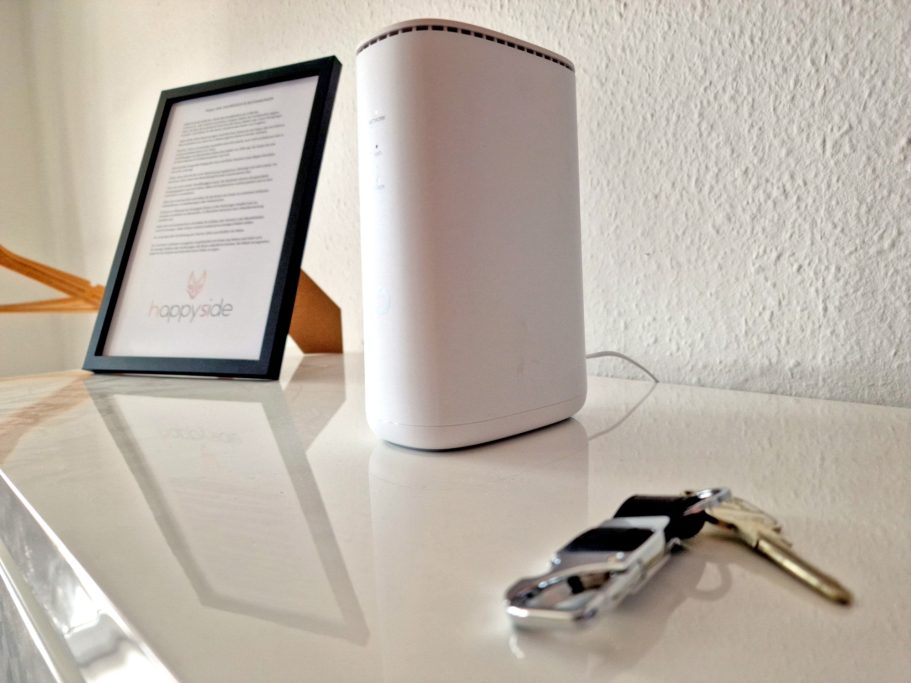 Wohnzimmer Weißes Router-Gerät auf einem Tisch, daneben ein Schlüsselbund und ein Tablet.