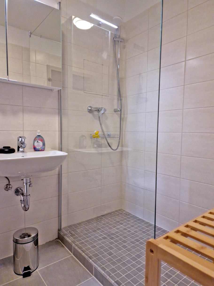 Bad Moderne Dusche in einem hellen Badezimmer mit Fliesen und Holzregal.