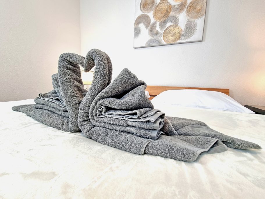 Schlafzimmer groß Zwei kunstvoll gefaltete graue Handtücher in Form von Schwänen auf einem Bett.
