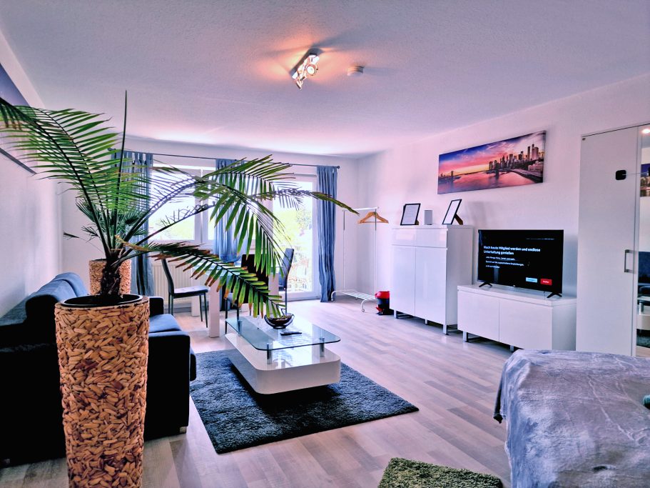 Wohnzimmer Moderner Wohnraum mit Pflanzen, Couch, Fernseher und dekorativen Elementen.