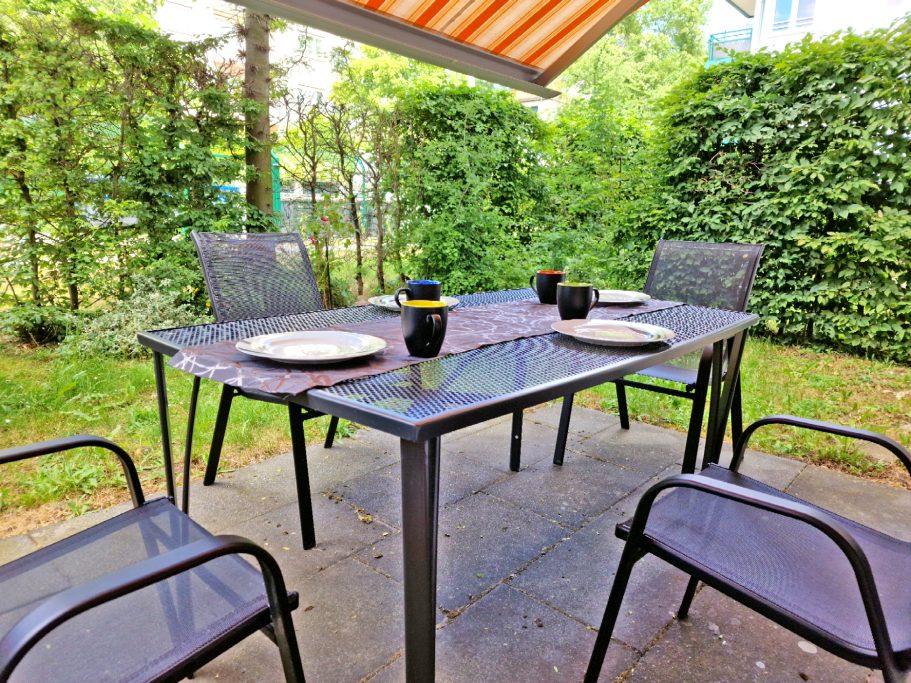 Terasse Ein gedeckter Tisch mit Stühlen im Garten, umgeben von grünen Büschen.