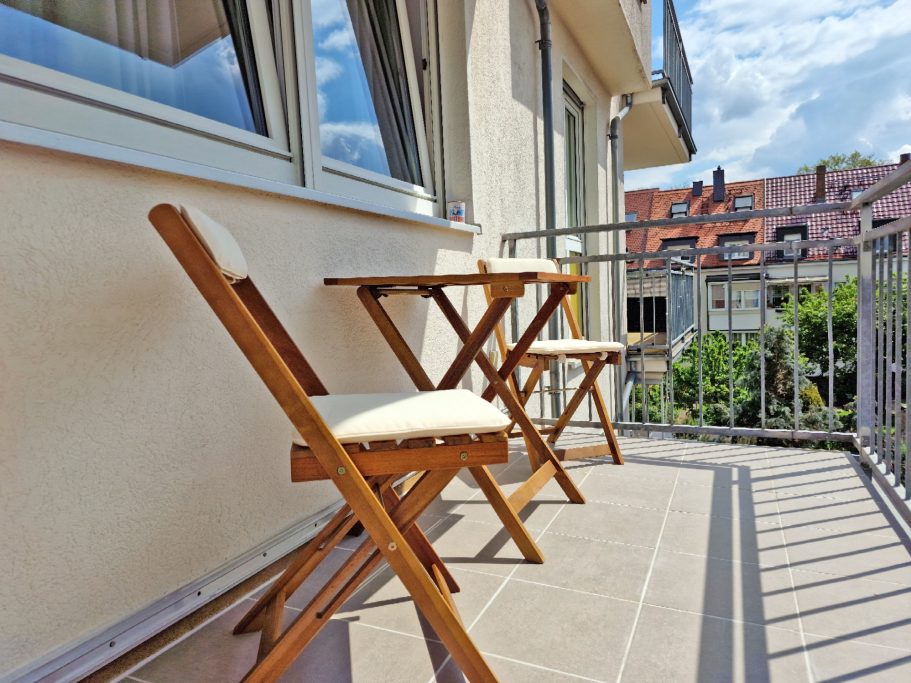 Balkon Balkon mit zwei Holzmöbeln und Blick auf ein Nachbarhaus und die Umgebung.