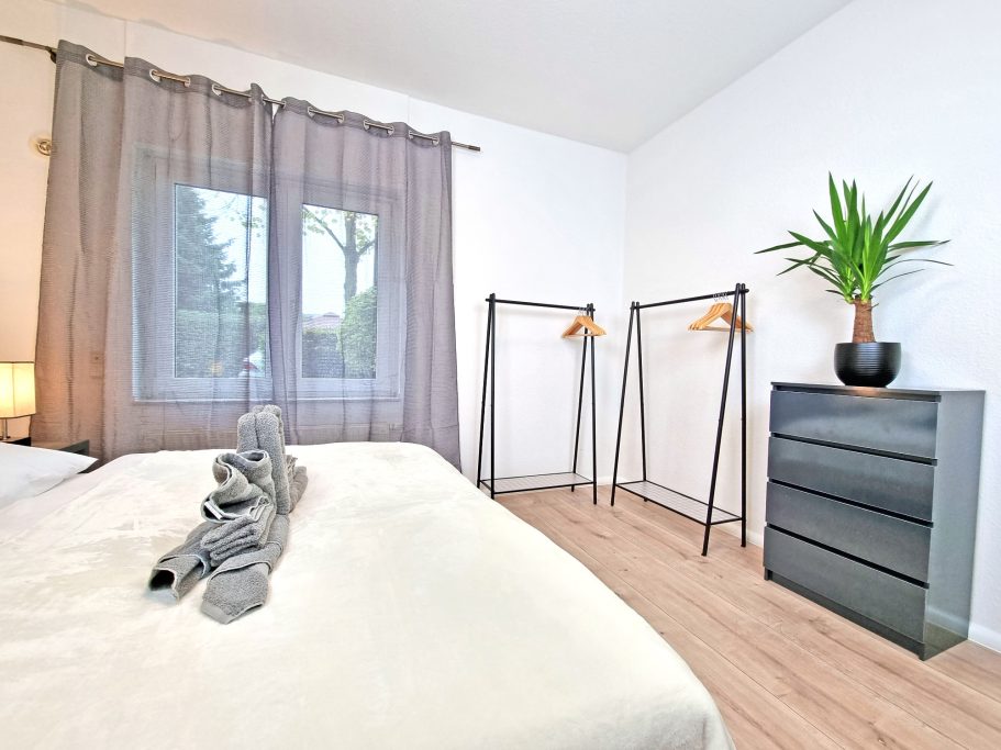 Schlafzimmer groß Helles Schlafzimmer mit Bett, Kleiderständern und einer Pflanze im Topf.