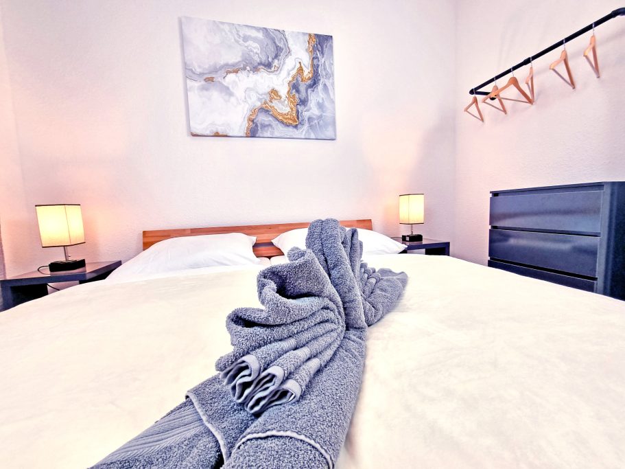 Schlafzimmer klein Bett mit grau-weißem Handtuch und modernen Lampen in einem hellen Raum.