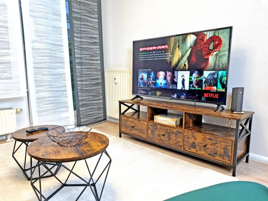 Wohnbereich Wohnzimmer mit Fernseher und zwei runden Holztischen. Helle, freundliche Atmosphäre.