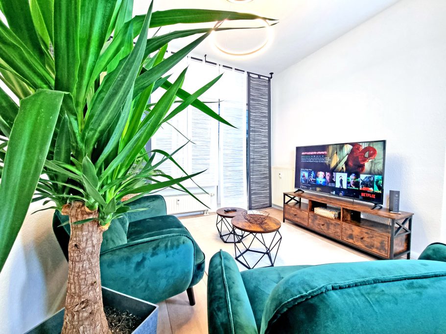 Wohnbereich Wohnbereich mit grüner Pflanze, modernen Möbeln und einem Fernseher an der Wand.