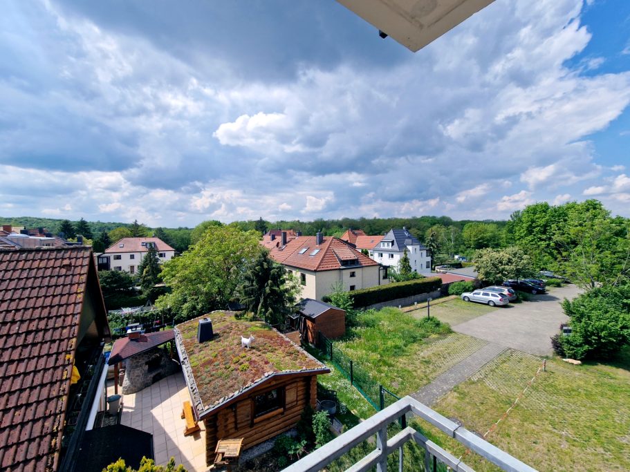 Blick vom Balkon Blick auf eine Wohngegend mit Häusern, Bäumen und einem Parkplatz unter bewölktem Himmel.